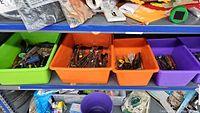 Assorted hand tools in green, orange, purple plastic bins on shelf