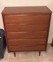 Front view of the walnut-colored wooden dresser showing five closed drawers and tapered legs.