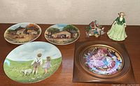 Full lot showing four decorative plates and two figurines on wood surface.