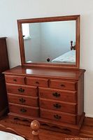 Front view of the solid maple dresser with nine drawers and an attached rectangular framed mirror, showing the natural wood finish and metal handles.