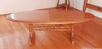 Side view of the solid maple oval coffee table showing the smooth tabletop and turned legs with crossbars.