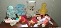 Photo of 8 plush toys including blue elephant, white bear with bow, yellow bird, and Mickey/Minnie Mouse plush toys.