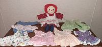 Raggedy Ann doll seated with five colorful dresses