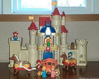 Front view of beige plastic toy castle with all included figures, horses, carriage, and throne arranged in front