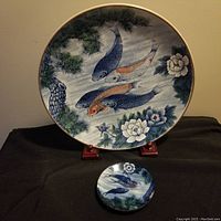 Large 16 inch decorative Japanese koi fish plate with small matching plate in front on black surface. Plates display colorful hand-painted style with koi fish, pine branches, and flowers. Stand is not included.