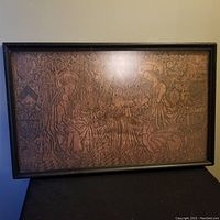 Full shot of the framed antique wood rubbing with religious imagery shown on table surface.