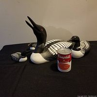 Wide shot of all four hand-carved loon decoys arranged on a black cloth surface alongside a Campbell's soup can for scale