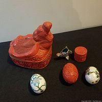 Full view of Chinese decorative lot showing red cinnabar carved bird box, small cinnabar container, cinnabar egg, cloisonné animal vessel, and two cloisonné eggs.