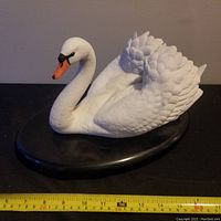 Porcelain bisque swan figurine side view showing the full body, white feathers, orange beak, and black base with measuring tape indicating length of 12 inches.