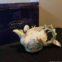 Front view of boxed Kathy Ireland Home by Franz swan teapot on black cloth
