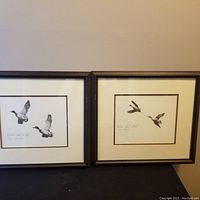 Two framed geese prints side by side against wall
