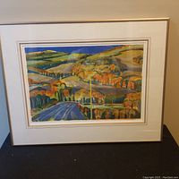 Full view of the framed colorful landscape print with trees and rolling hills in autumn tones of orange, yellow, and blue sky.