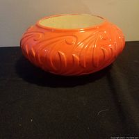 Orange ceramic bowl with raised swirling leaf motif, cream interior, shown from side angle.
