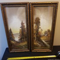 Pair of framed antique pastel paintings showing landscape scenes with trees, water, and a house, with tape measure for size reference