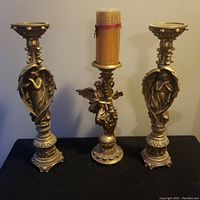 Three vintage angel pillar candle holders in gold-tone finish displayed on black surface