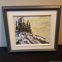 Frontal view of the oil painting showing pine trees on rocky hill with yellow cloudy sky, framed in gray with white mat.