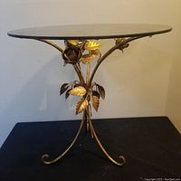 Side view showing ornate metal floral base and round glass top