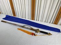 Full sword with scabbard and yellow tassel laying beside blue nylon cover
