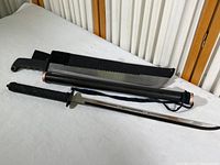 Photo showing the full set of decorative samurai accessories on white cloth background: sword, machete, and their sheaths.