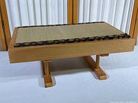 Photo showing a full view of the rectangular wooden floor table with tatami mat top and decorative border, placed indoors with natural light through curtains in background.