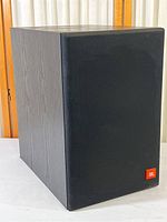 Front view of the JBL subwoofer with grille covering the speaker cone. Shows logo placement and cabinet finish.