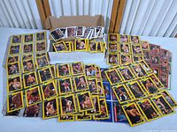 Wide view showing numerous WCW wrestling cards spread out on the table and a box filled with loose wrestling cards.