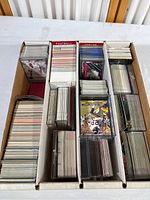 Wide shot of multiple stacks of mixed trading cards in storing box. Cards include sports and entertainment themes.