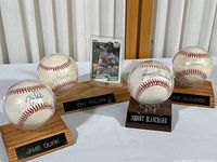 Photo of four autographed baseballs on wooden stands and one autographed Tony Phillips baseball card standing upright in center.