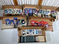 Six cardboard boxes filled with loose baseball cards, some cards laid out on top including different card backs and fronts showing various players and card sets.