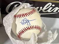 Single baseball removed from box showing blue ink autograph (Mark McGwire) on white leather ball with red stitching.