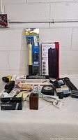 View of various office supplies including surge protectors, batteries, pens, work light, and other tools on a white table against a wall.