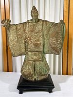 Front view of plaster figurine showing full figure of a Chinese man in traditional robes with outstretched arms, wearing a pointed hat, on black rectangular base.