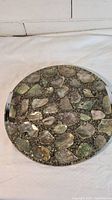 Front view of round resin serving tray showing inlaid stones or shell pieces embedded in the glossy resin surface with metal handles on each side.