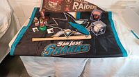 Photo showing a San Jose Sharks flag laid out with assorted Bay Area sports memorabilia including miniature baseball bats, Giants baseball ornaments, pins, and a miniature football.