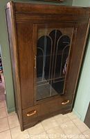 Front view of the solid wood display cabinet showing glass door and drawer with wooden handles.