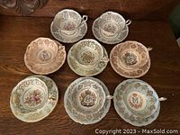 Eight pastel teacup and saucer sets laid out on wooden surface