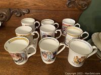 Front view of all nine royal themed mugs arranged together showing various portraits and royal crests with gold trim