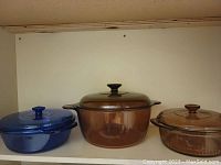 Three glass pots on a white shelf, two amber-colored and one blue-colored