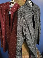 Two XL Ben Sherman shirts hanging side by side on white plastic hangers against a blue door background. One shirt is red with a small white pattern, the other is black with a white pattern.
