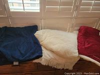 Three blankets laid out: navy blue, white textured with fringe, and burgundy sherpa lined.