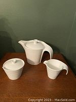 Set of Bowring teapot, creamer, and sugar bowl displayed on a wooden surface against a green background.