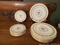 Set of 8 Coalport plates arranged on table: 6 smaller plates stacked and 2 larger plates displayed on stands, showing the floral urn and blue decorative border pattern with gold trim.