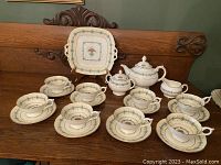 Full display of teapot, sugar bowl, cream pitcher, cake plate, cups and saucers on wooden bench