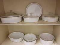 Shelved white Corning French White bakeware including multiple casserole dishes and plates, some with clear glass lids.