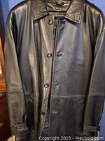 Front view of black leather jacket with button closure, collar, front pockets, and cuff button straps.
