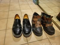 Photo showing the pair of black leather shoes and brown/black winter boots side by side on tiled floor