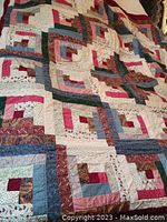 Full view of quilt showing patchwork design with log cabin blocks in various patterned fabrics, primarily in red, blue, and beige tones.