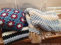Photo showing one crocheted cushion and two crocheted blankets with different color schemes.