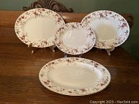 Four oval serving platters displayed standing on wooden stands, showing floral decoration with red and blue flowers and brown vines along scalloped edges.