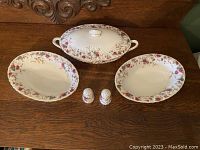 Full set arranged on wooden surface showing the covered vegetable serving dish with lid, two open vegetable bowls, and salt and pepper shakers with floral pattern.